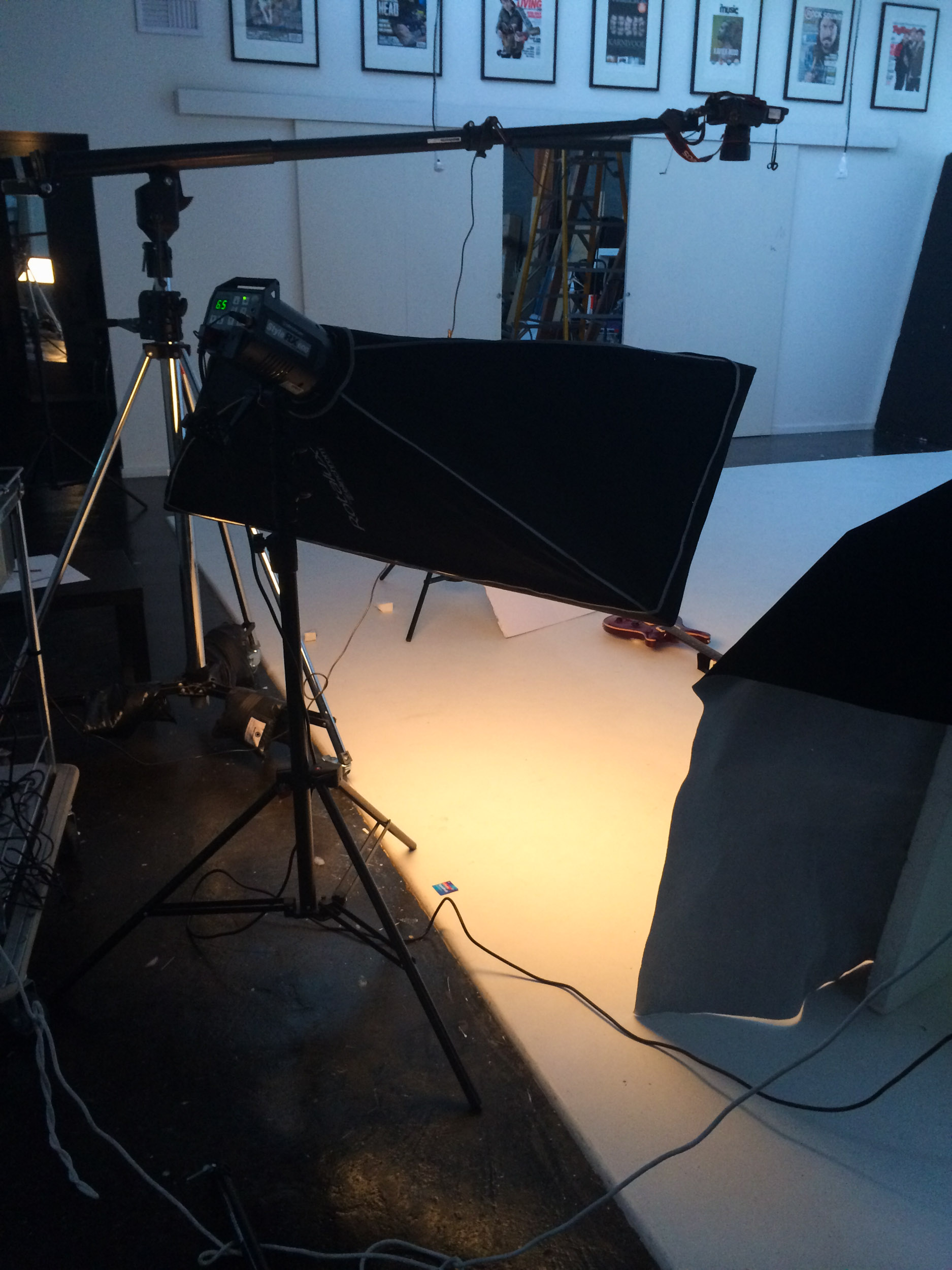 Photographic lights reflect on a white floor and guitar is seen lying flat in the top corner.