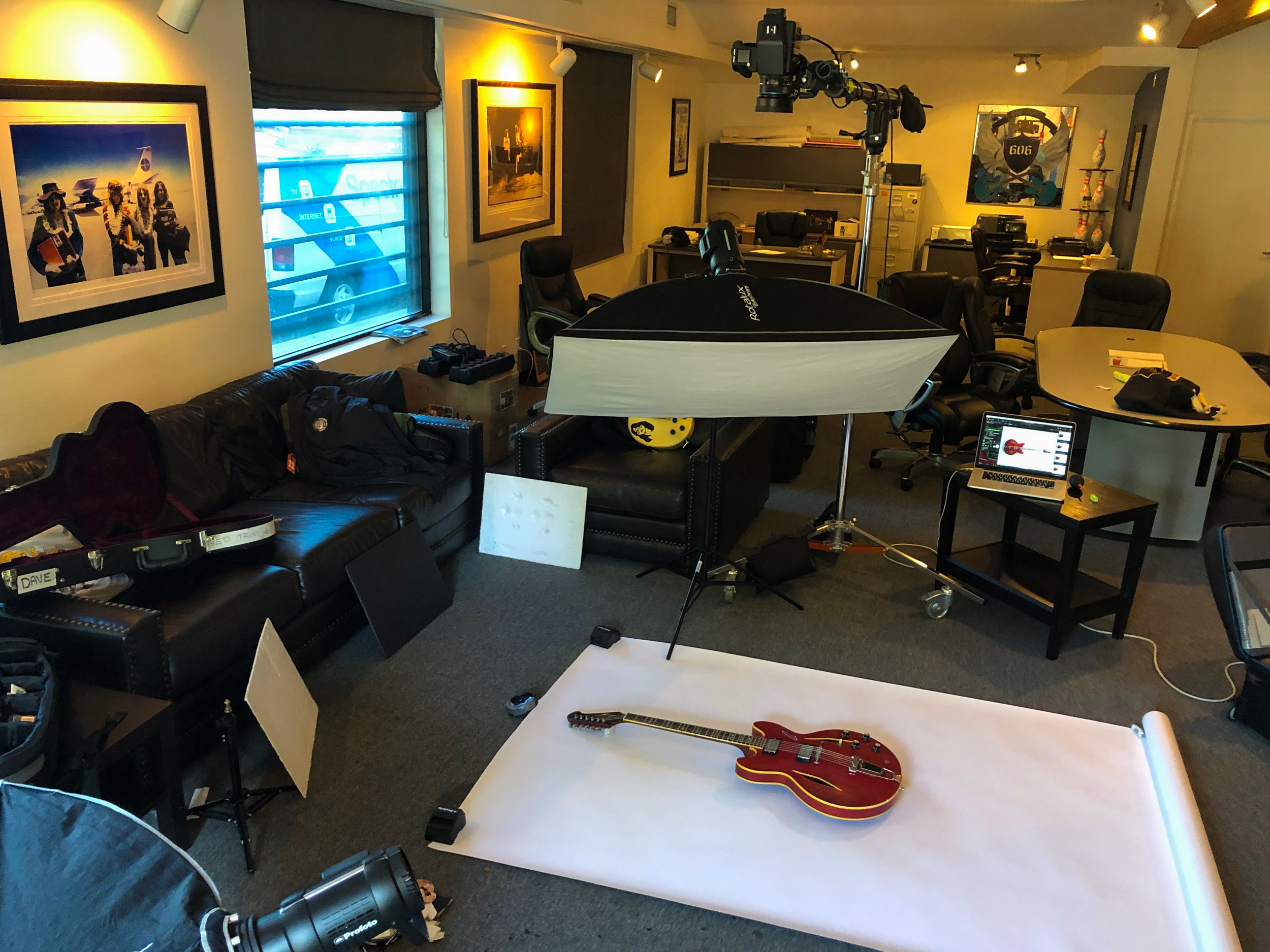 Photographic set up with guitar on white background on floor surrounded by lights and equipment.