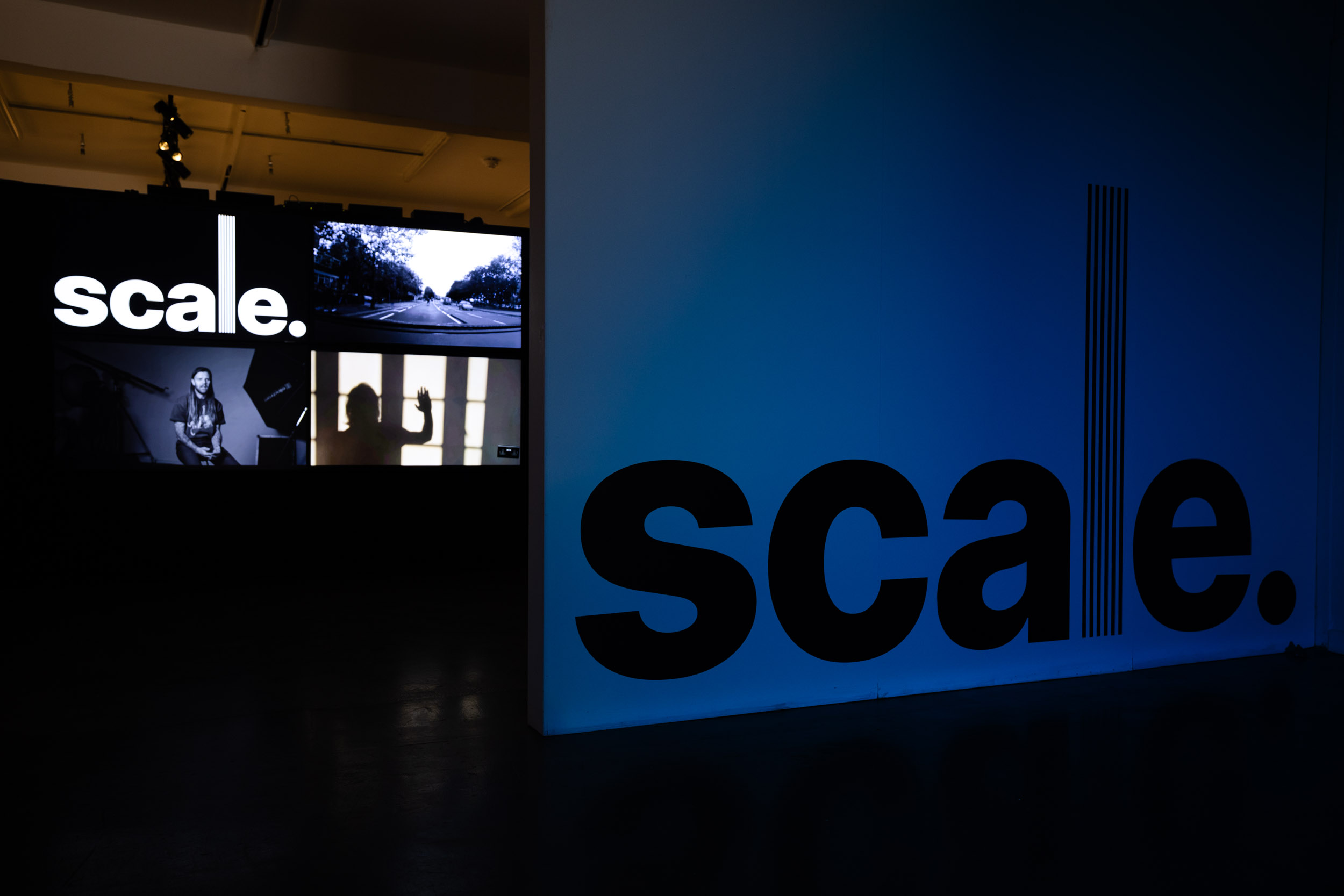 Four video screens are mounted on a black wall. The screens display logo and still images in a montage.