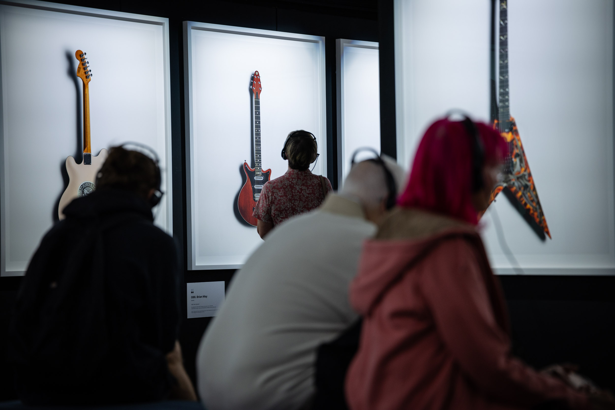 People look at images of guitars in white frames while using headphones to hear their stories.
