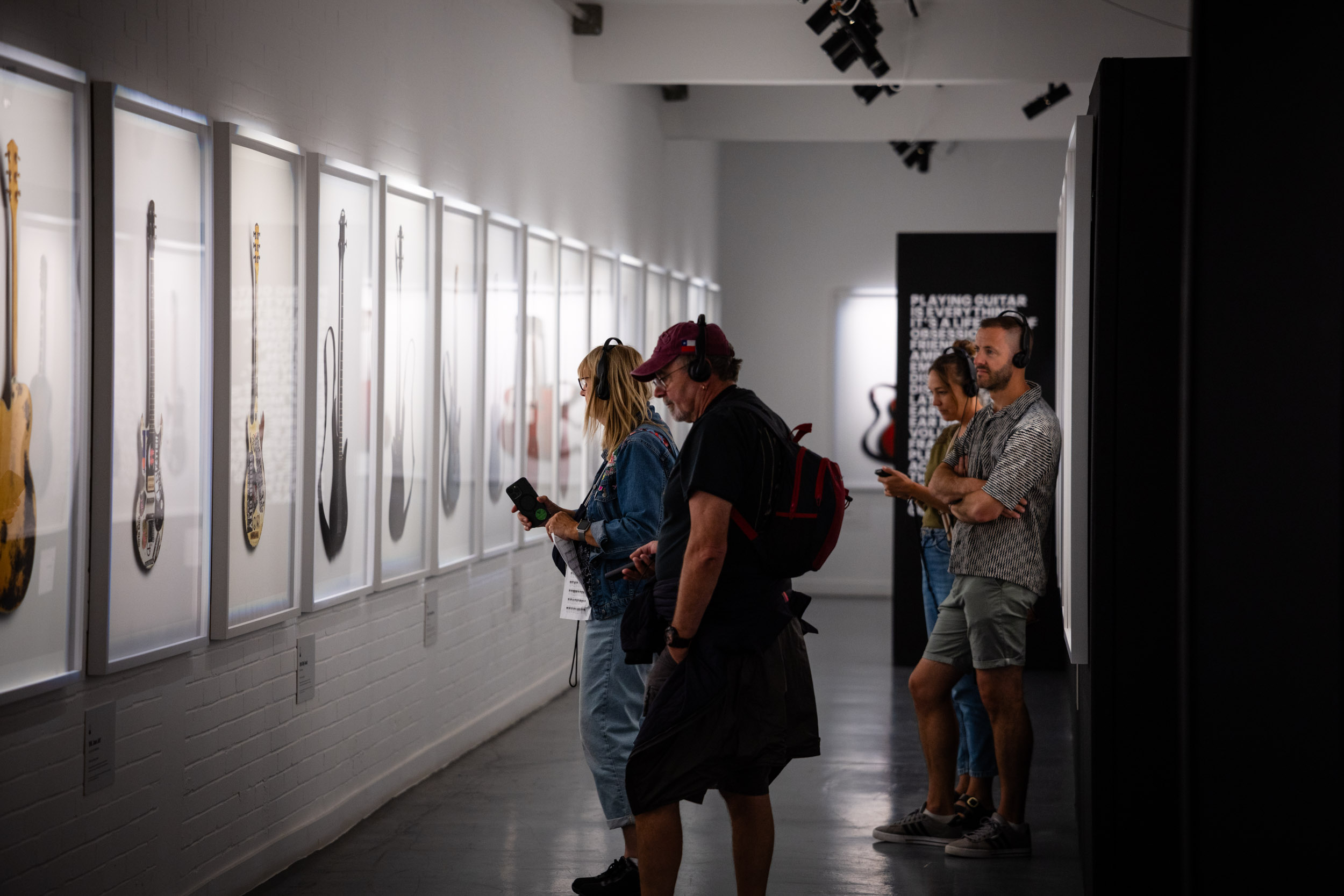 People look at images of guitars in white frames while using headphones to hear their stories.